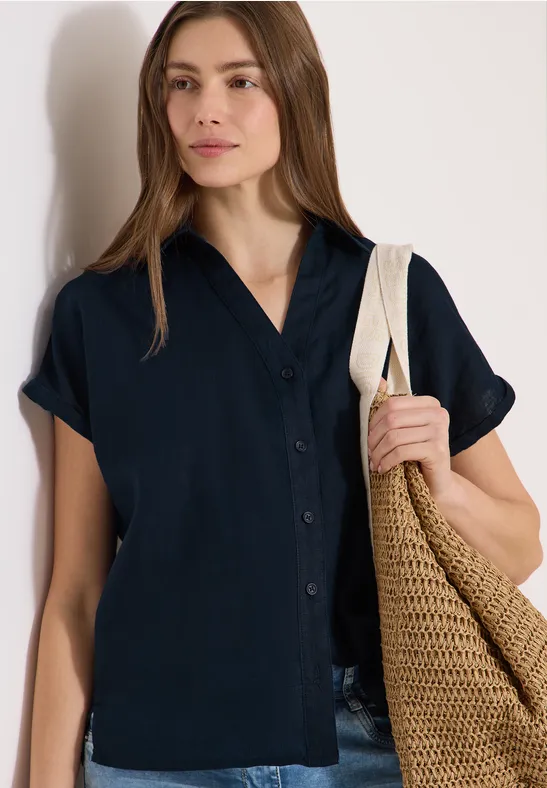 Frau in schwarzer, kurzärmeliger Bluse mit gehäkelter Einkaufstasche über der Schulter