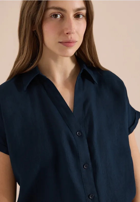 Porträt einer Frau in einem navyblauen Kurzarm-Hemd mit offenem Kragen.