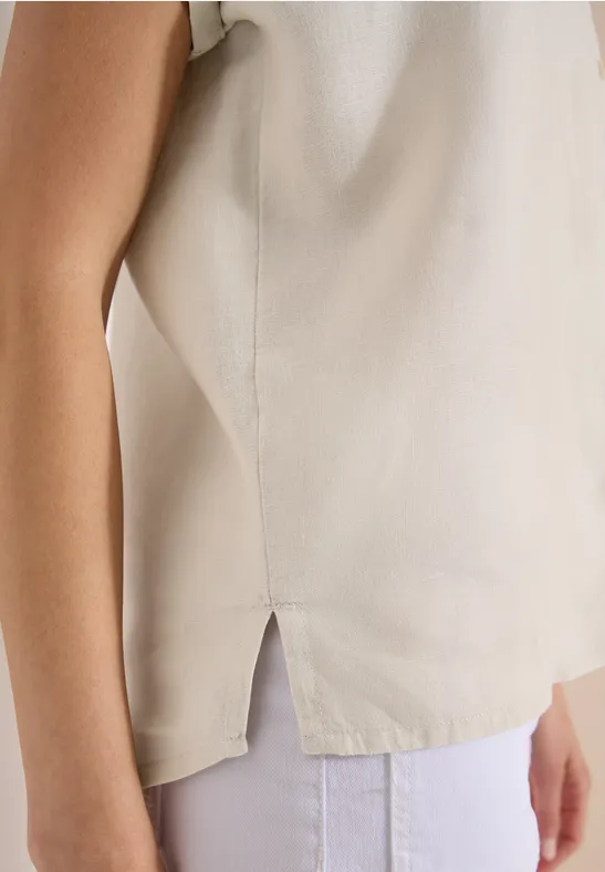 Seitliches Detail eines beige Tops mit Schlitz, getragen zu weißen Hosen.