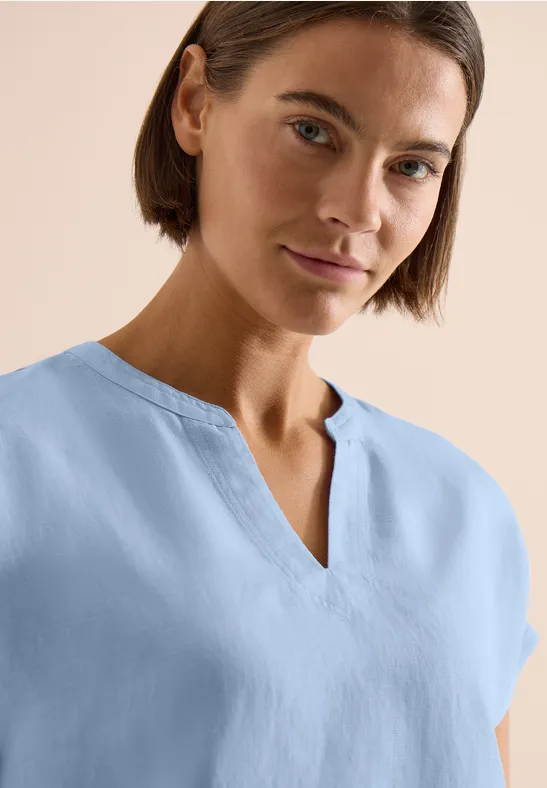 Frau mit pastellblauem Shirt und V-Ausschnitt vor hellem Hintergrund.