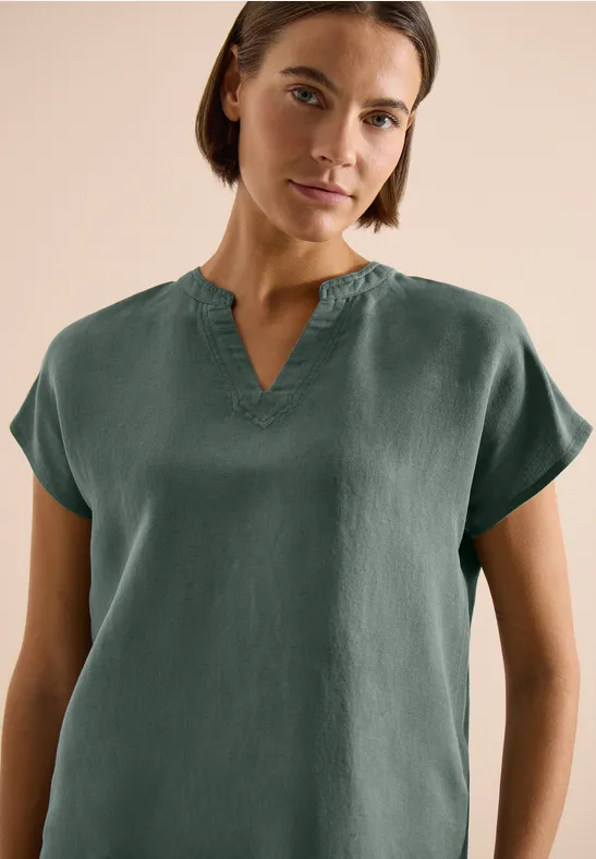 Frau trägt dunkelgrünes, kurzärmeliges Oberteil mit V-Ausschnitt.