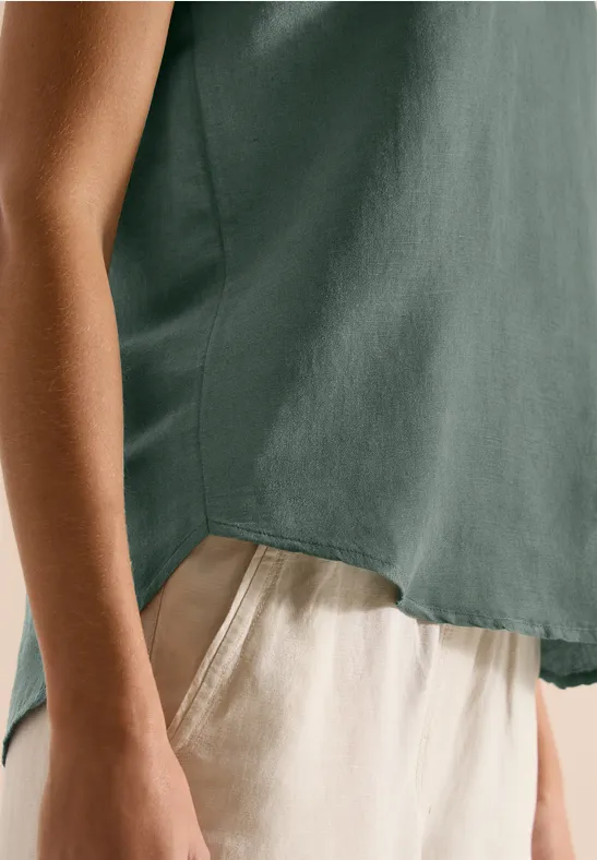 Seitliche Ansicht einer Person in lockerem grünen Top und hellen, beigen Hosen.