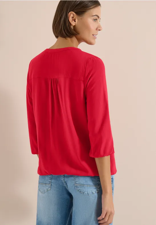 Frau von hinten in roten 3/4-Ärmel-Shirt und blauen Jeans vor hellem Hintergrund