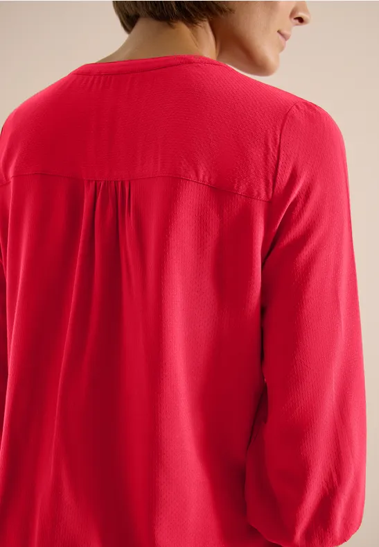 Ansicht einer Person von hinten in rotem, langärmligem Oberteil.