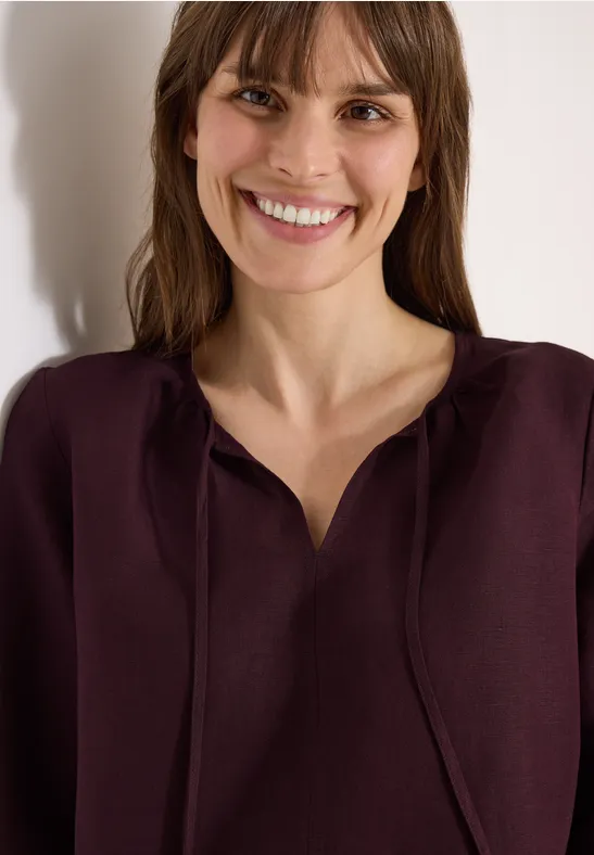 Frau mit weinrotem Oberteil, verschwommenem Gesicht und offenem Haar, Schulteransicht vor hellem Hintergrund.