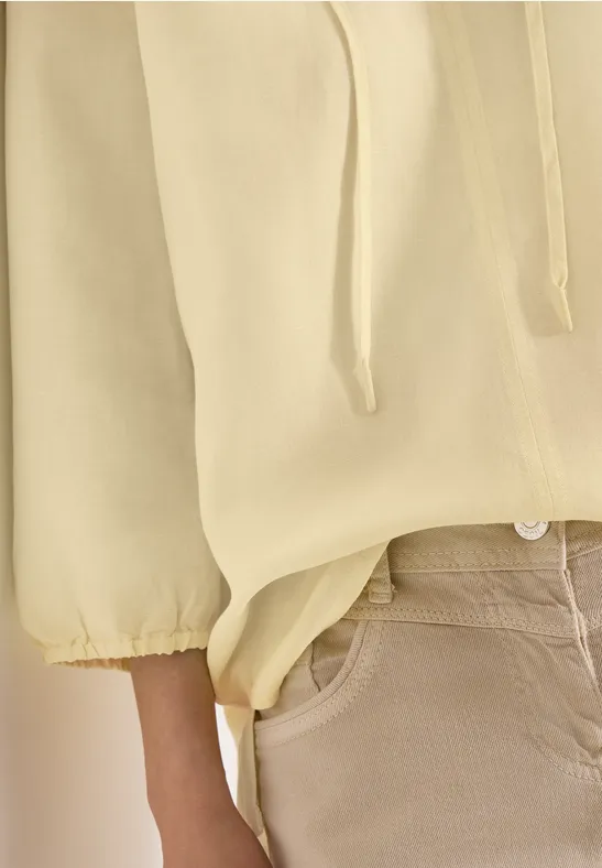 Nahaufnahme einer Person in gelbem Pullover mit Kordelzug und beigen Hosen.