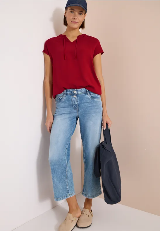 Frau in roter Bluse, weiten hellblauen Jeans und beigen Schuhen trägt eine dunkelblaue Tasche.