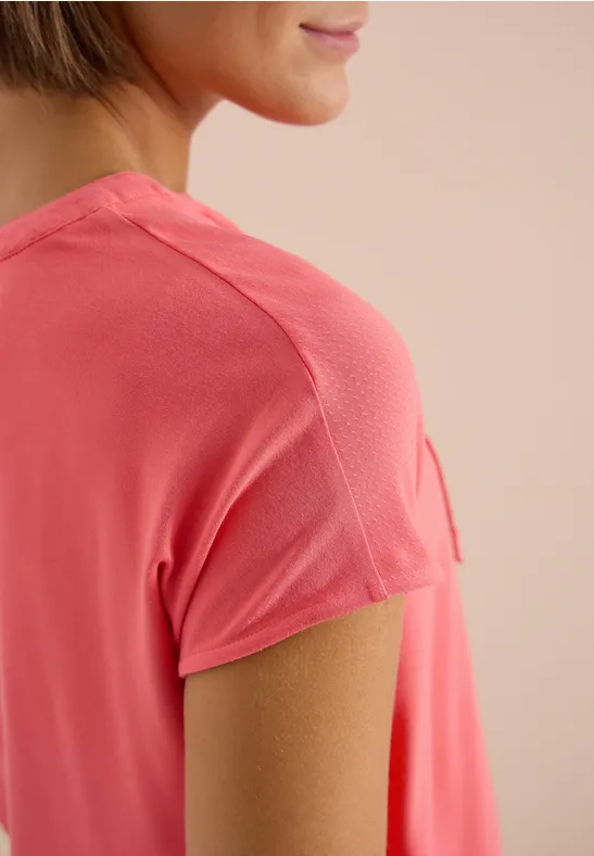 Nahaufnahme einer Frau in einem korallfarbenen T-Shirt, Fokus auf Schulter und Ärmeldetail.