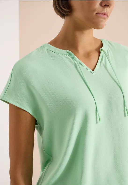 Kort damestop in lichtgroen met capuchon en trekkoord.