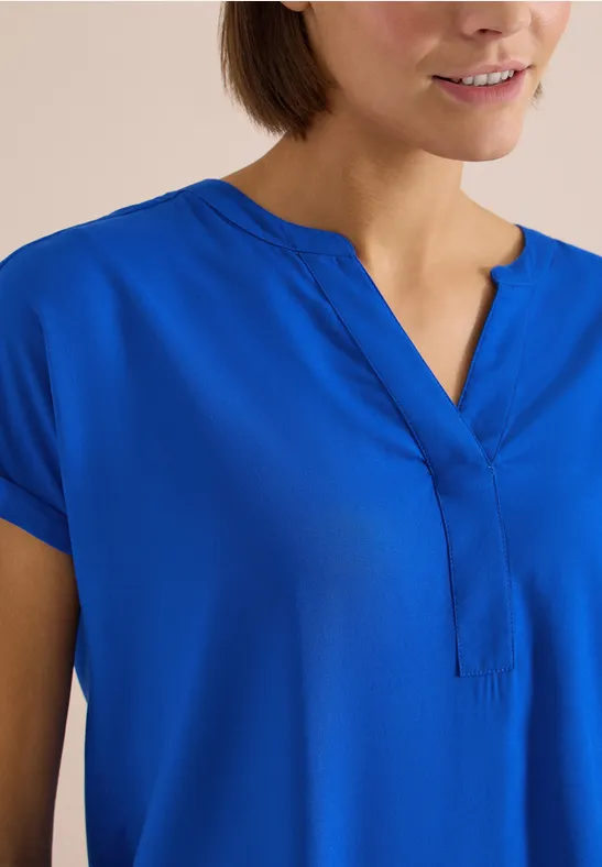 Frau in leuchtend blauer Bluse mit kurzen Ärmeln und V-Ausschnitt