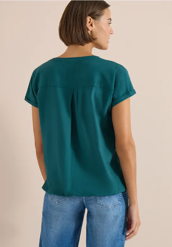 Een vrouw van achteren in een groen t-shirt en een blauwe spijkerbroek.