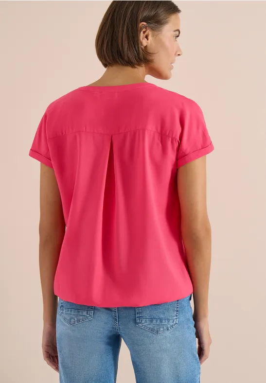 Vrouw van achteren in een felroze blouse met korte mouwen en spijkerbroek voor neutrale achtergrond.