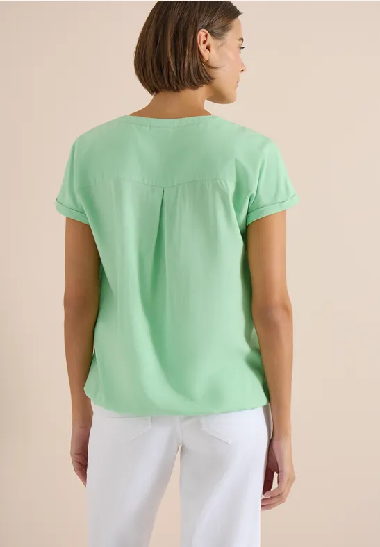 Vrouw van achteren in mintgroene blouse met korte mouwen en witte broek.