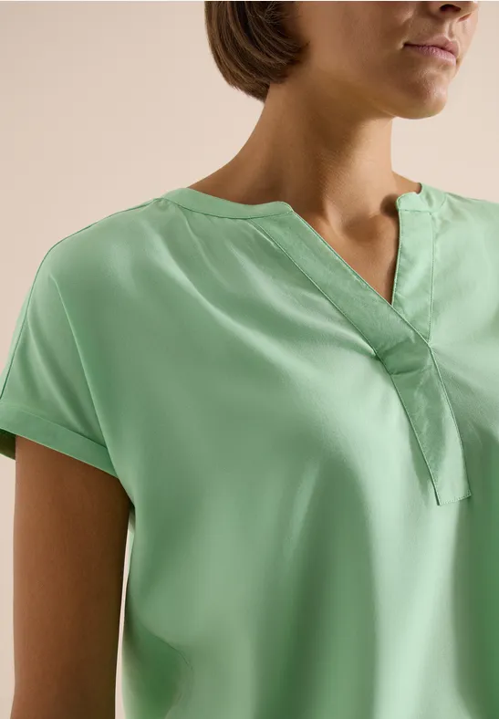Een persoon draagt een lichtgroene blouse met V-hals.
