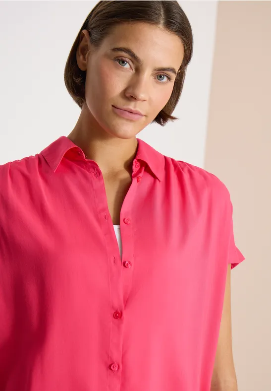 Een persoon met vaag gezicht draagt een felroze overhemd met korte mouwen en knoopsluiting.