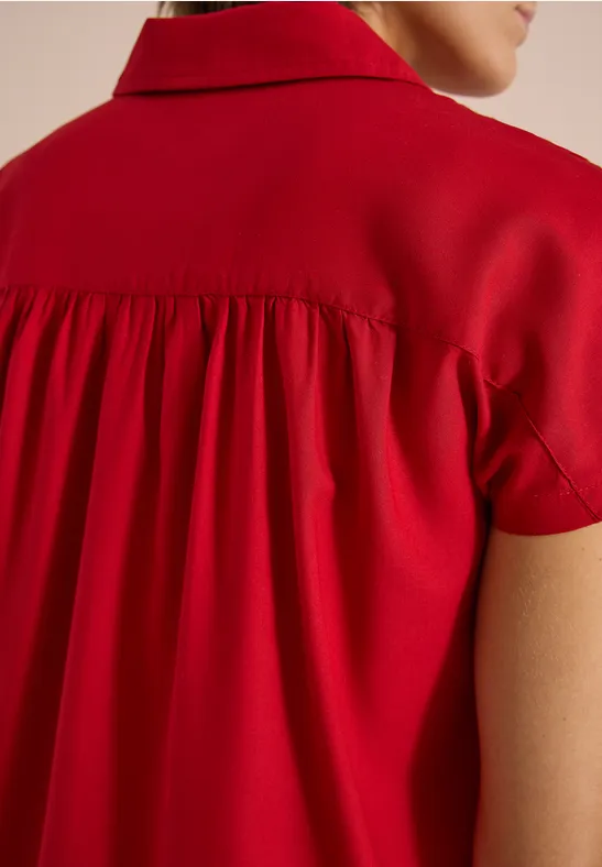 Gros plan du dos d’une blouse rouge avec fronces au niveau de l’épaule.