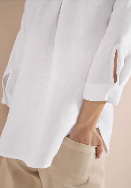 Weiße Bluse mit 3/4-Ärmeln und beigen Hosen, Hand in Hosentasche.