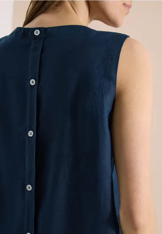 Une femme de dos porte une robe sans manches bleu marine avec une boutonnière centrale dans le dos.