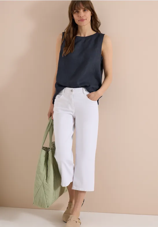 Femme porte un haut bleu marine, un pantalon court blanc et un sac vert.