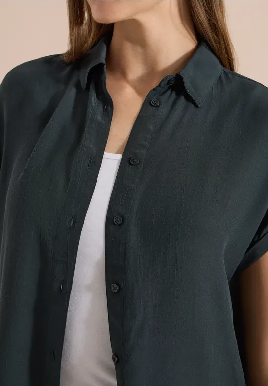 Une personne porte une chemise sombre à manches courtes sur un débardeur blanc.