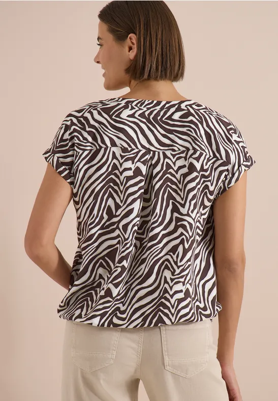 Frau von hinten in kurzärmeligem, schwarz-weißem Zebraprint-Oberteil und hellen Hosen.