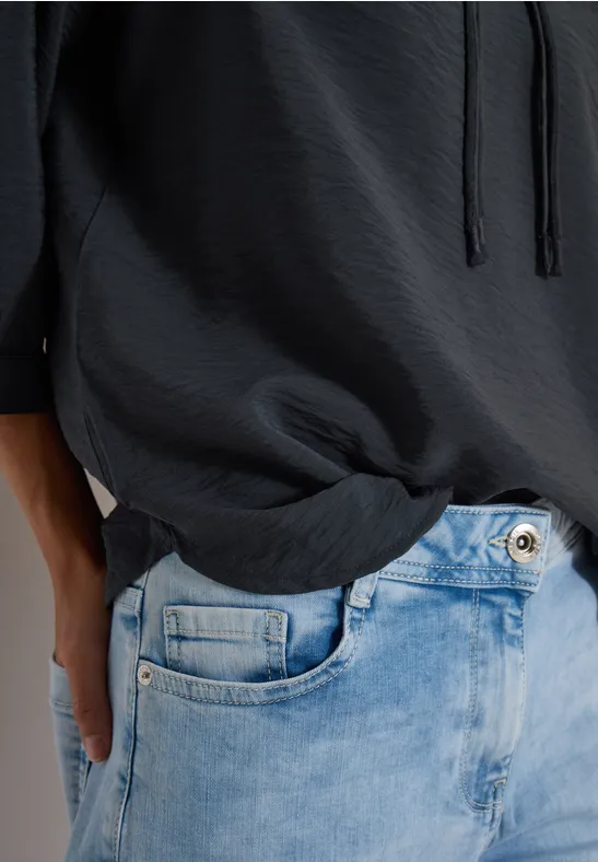 Person trägt schwarzen Kapuzenpulli und hellblaue Jeans, Hand in Hosentasche.