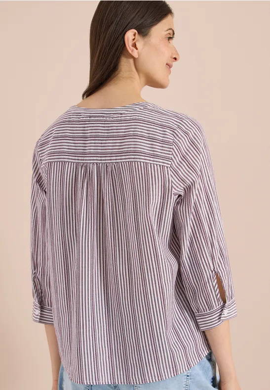 Rückansicht einer Person mit gestreifter Bluse und hochgekrempelten Ärmeln.