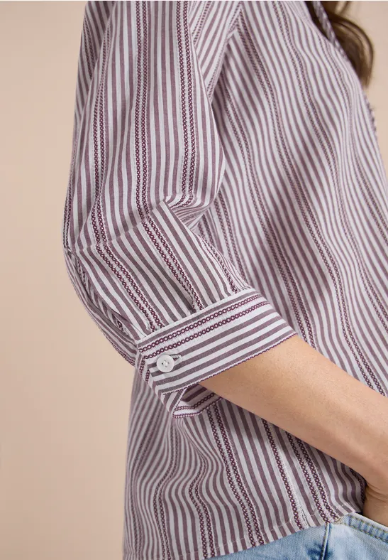 Nahaufnahme eines gestreiften Hemdes mit hochgekrempeltem Ärmel, kombiniert mit Jeans.