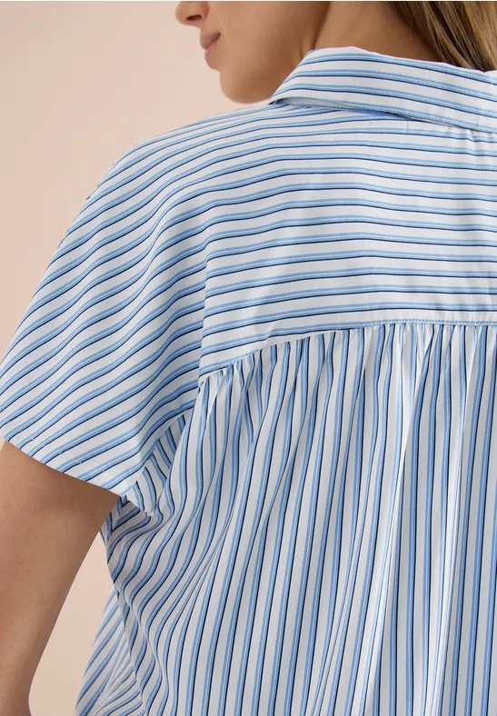Rückenansicht einer Frau in leichtem, kurzärmligem Hemd mit blauen und weißen vertikalen Streifen.