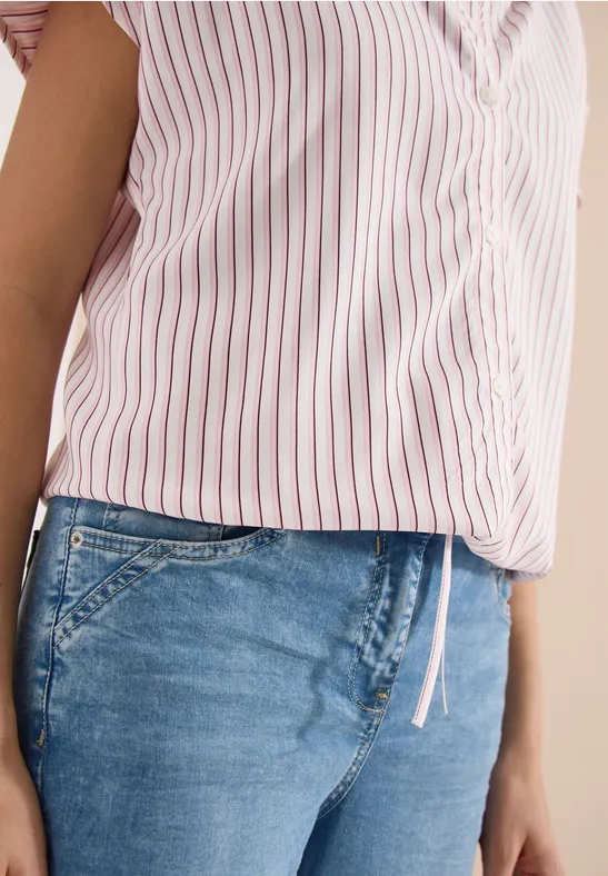 Eine Person trägt eine rosa-weiß gestreifte Bluse und blaue Jeans.