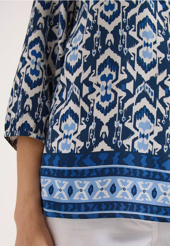 Frau trägt blau-weiß gemustertes Oberteil mit 3/4-Ärmeln und dekorativem Saum