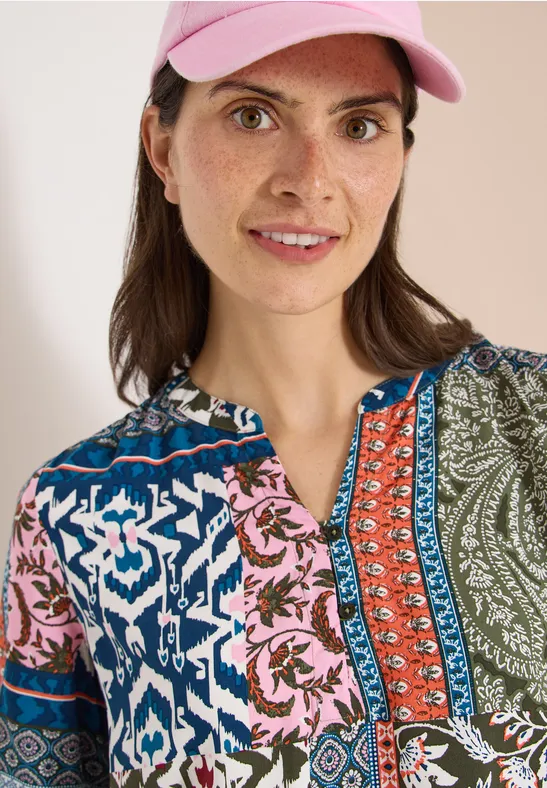 Dame mit rosa Baseballcap und bunter Patchwork-Bluse, Gesicht unscharf.