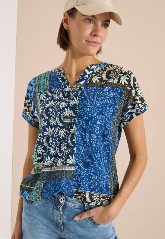 Eine leichte Patchwork-Bluse mit blau-weißem Paisley- und Blumenmuster, kurzen Ärmeln und V-Ausschnitt.
