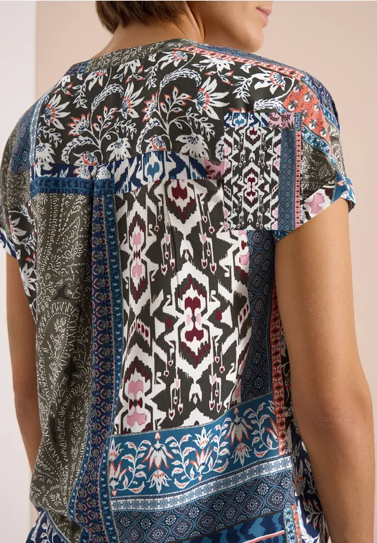 Vrouw van achteren in een kleurrijke patchworktop met bloem- en geometrische patronen.