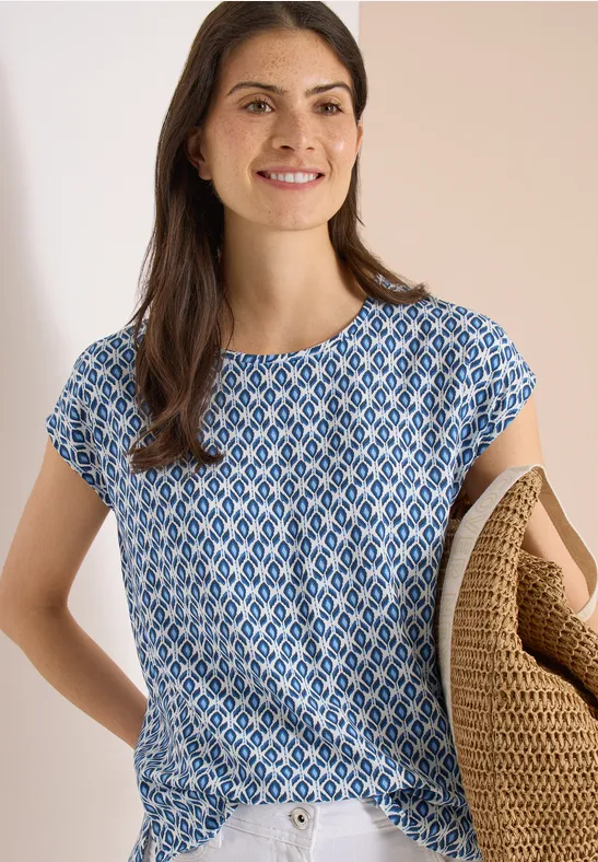 Frau trägt blau-weiß gemustertes T-Shirt und hält einen geflochtenen Korb in der Armbeuge.