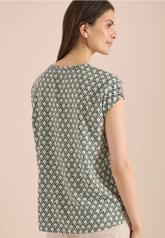 Rugaanzicht van een vrouw in een groen-witte, kortmouwe top met een geometrisch patroon.