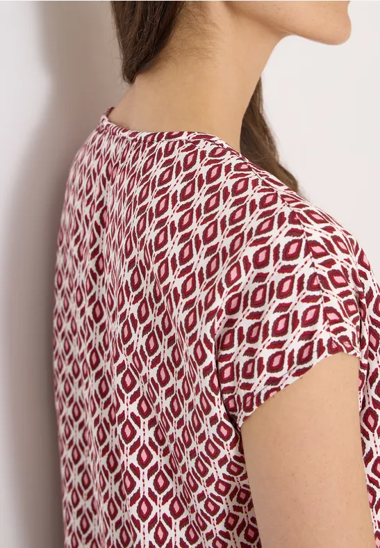 Zijaanzicht van een vrouw in een wit shirt met rood geometrisch patroon.