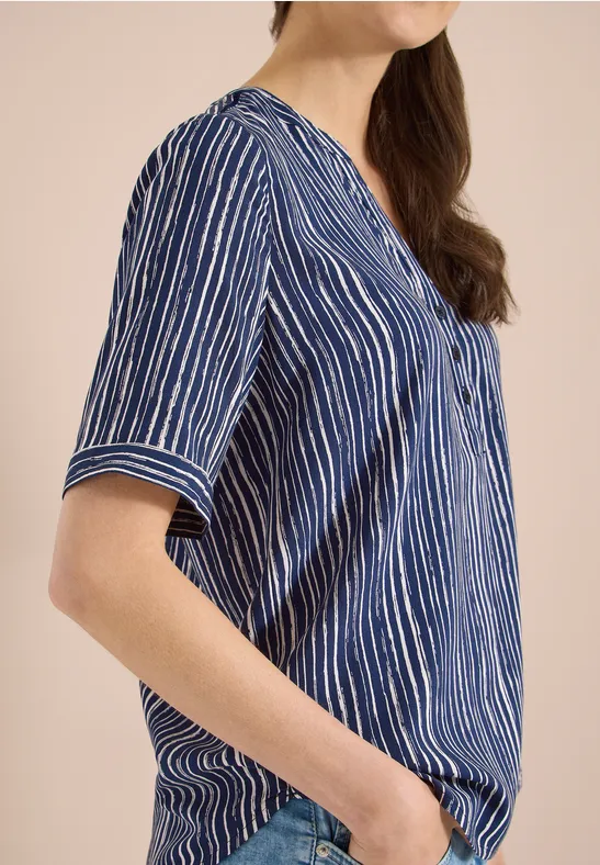 Eine Frau trägt eine kurzärmelige, blau-weiße, vertikal gestreifte Bluse mit V-Ausschnitt.