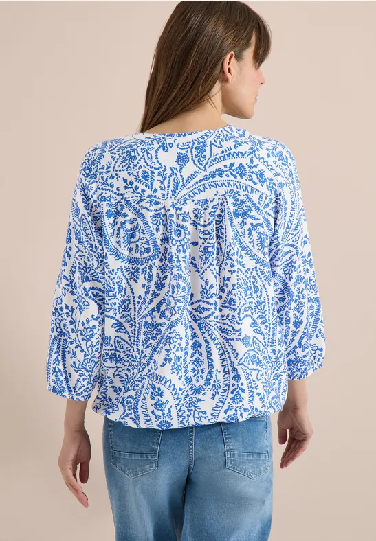 Frau von hinten in weißer Bluse mit blauem Paisley-Muster und Jeans.