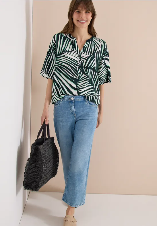 Frau trägt kurzärmliges Hemd mit grün-weißem Zebramuster, blaue weite Cropped-Jeans und schwarzen Flecht-Shopper.
