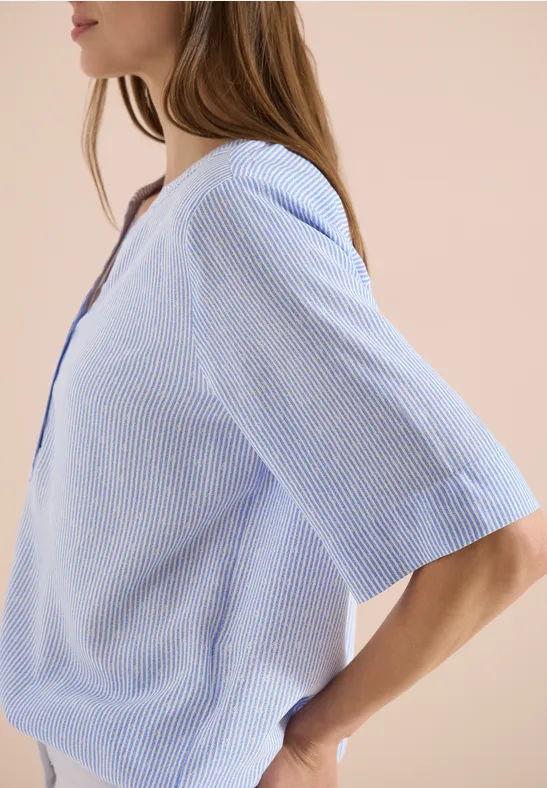 Zijaanzicht van een vrouw in lichtblauwe gestreepte blouse tegen een beige achtergrond.
