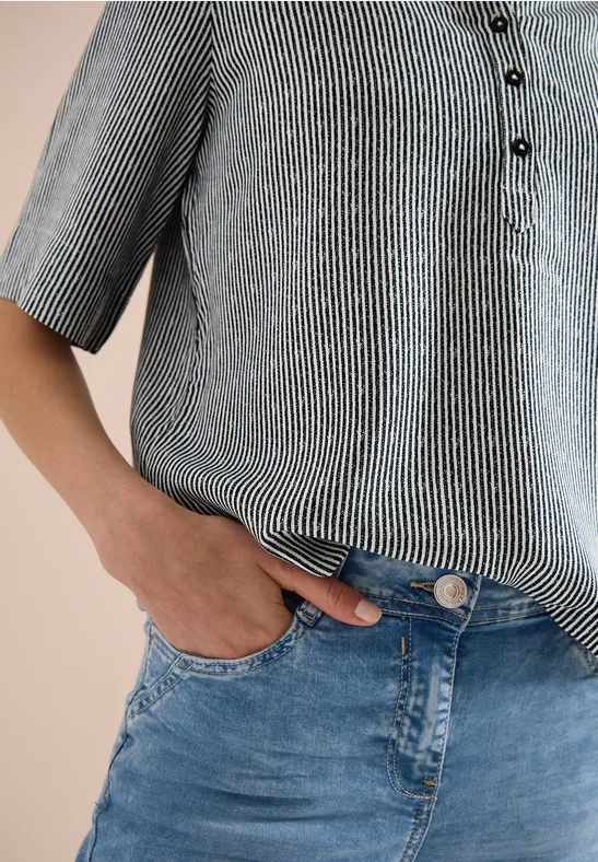 Eine Person trägt gestreiftes Hemd und blaue Jeans, Hand in der Hosentasche.