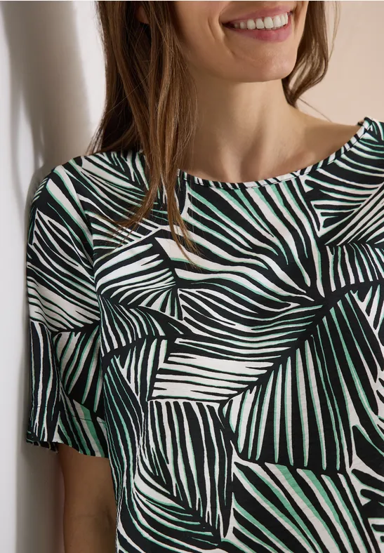 Nahaufnahme: Oberteil mit weiß-schwarzem Blättermuster und grünen Akzenten, Schulteransicht.