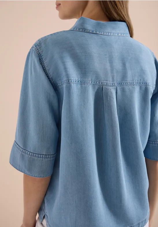 Achteraanzicht van iemand in een lichtblauw denimblouse met opgerolde mouwen.