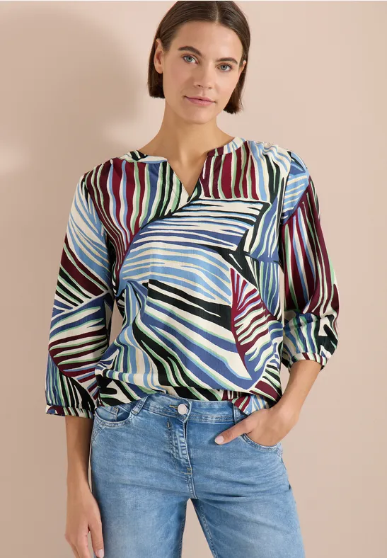Vrouw met een meerkleurig zebrapatroon blouse, 3/4 mouwen en V-hals, gecombineerd met een jeans.