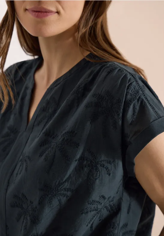 Frau trägt dunkle Bluse mit kurzem Arm und feinem Muster, Ausschnitt in V-Form.