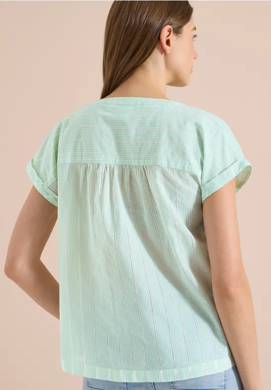 Femme de dos en blouse courte rayée vert clair, posture décontractée.