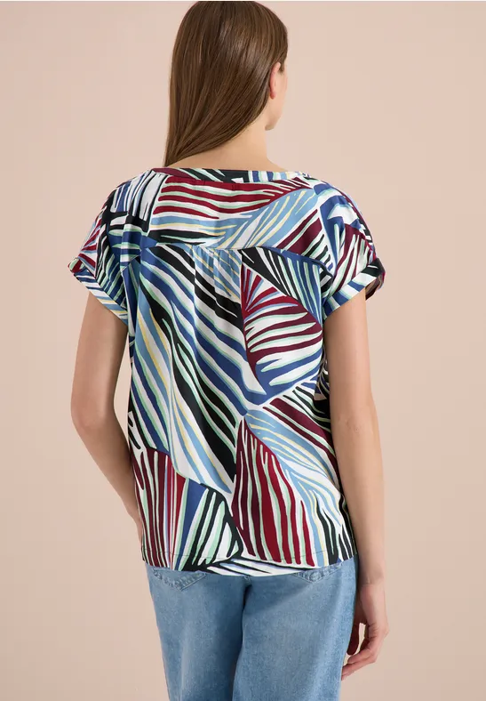 Vrouw van achteren in een losvallende, kleurrijk gestreepte top met korte mouwen, gecombineerd met een blauwe jeans.