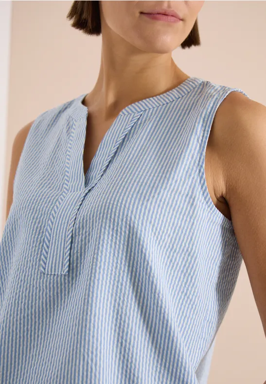 Femme portant un top sans manches bleu à rayures blanches, col fendu, sur fond clair.