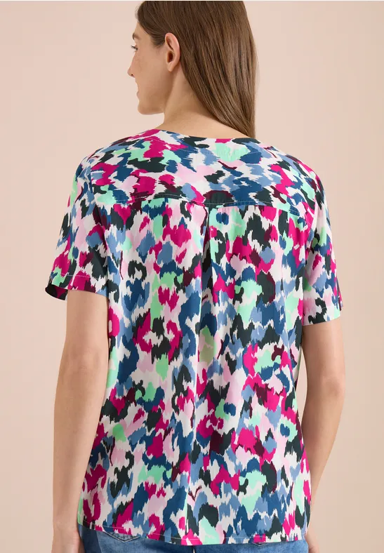 Vrouw van achteren met een kort mouws shirt met kleurrijk abstract patroon in roze, blauw, wit en zwart.